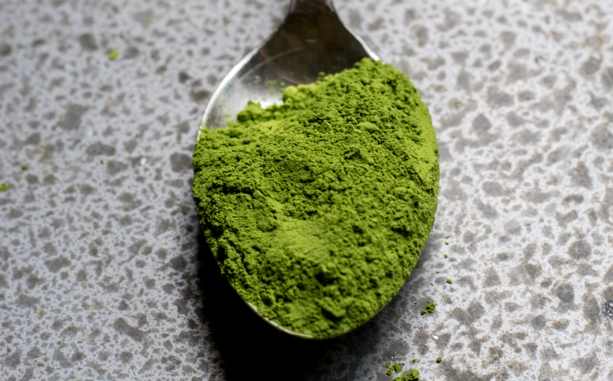 Close-up of a spoon filled with green powder placed on a stone countertop, showcasing a healthy supplement.