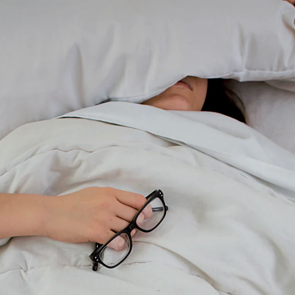 Peaceful woman sleeping in a white bed, cozy under soft covers with a relaxed expression, as natural light filters into the room.