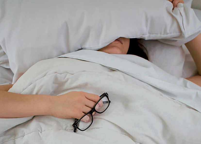 Peaceful woman sleeping in a white bed, cozy under soft covers with a relaxed expression, as natural light filters into the room.
