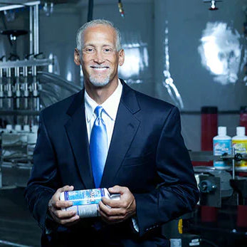 Dr. Richard Drucker in a suit, holding a bottle of intraMAX, representing his commitment to high-quality, natural supplements for optimal health and wellness.