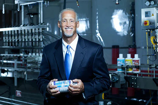 Dr. Richard Drucker in a suit, holding a bottle of intraMAX, representing his commitment to high-quality, natural supplements for optimal health and wellness.